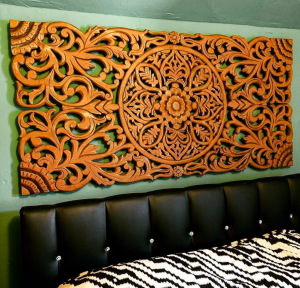 A long rectangle carved in an intricate floral design, hanging on the wall over a bed.
