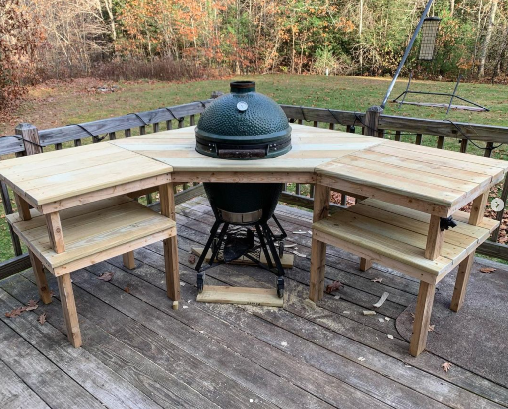 A sort of L shaped table built around a Big Green Egg grill, out on a back deck.
